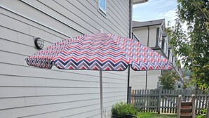 Une terrasse extérieure avec une table et des chaises, un parasol à motifs et une clôture en bois en arrière-plan.