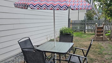 An outdoor patio with a table and chairs, a patterned umbrella, and a wooden fence in the background.