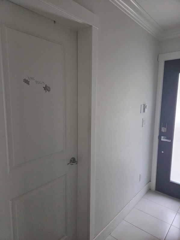 A hallway with a white door labeled 'THE ROOM' and a dark-colored door at the end.