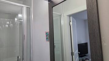 A bathroom with a glass shower enclosure and a door leading to a room with a television.
