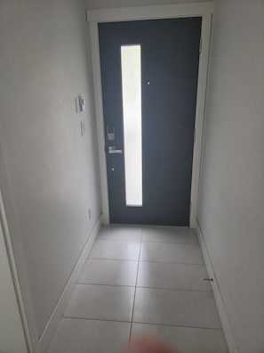 A hallway with a dark door, white walls, and a tiled floor. - Serene 1-bedroom townhome in welcoming Surrey neighborhood (Surrey)