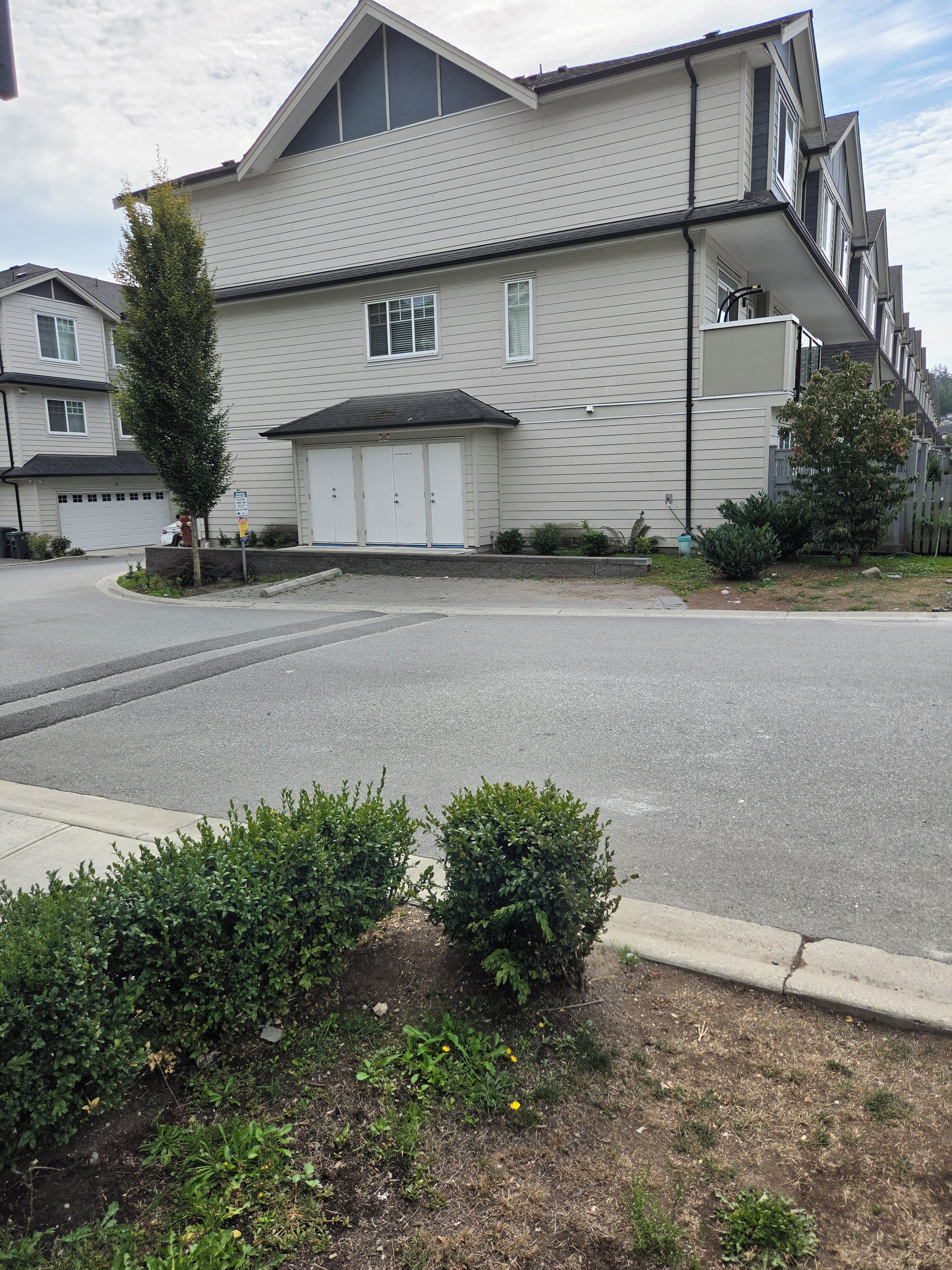 A residential building with a garage, a driveway, and a small garden area with bushes.