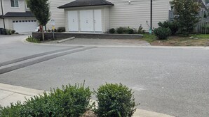Un immeuble résidentiel doté d’un garage, d’une allée et d’un petit jardin agrémenté d’arbustes.