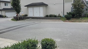 A residential building with a garage, a driveway, and a small garden area with bushes.