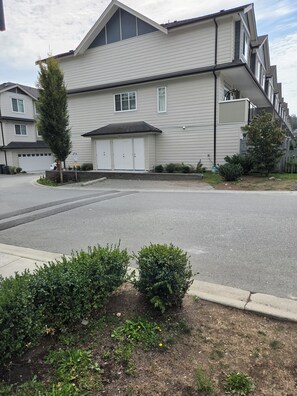 A residential building with a garage, a driveway, and a small garden area with bushes. - Serene 1-bedroom townhome in welcoming Surrey neighborhood (Surrey)