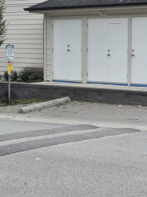 A building with a garage door, a sign indicating authorized parking, and a warning sign for high voltage.