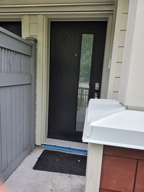 A black door with a keypad lock, a grey fence, and a concrete step leading to a driveway.