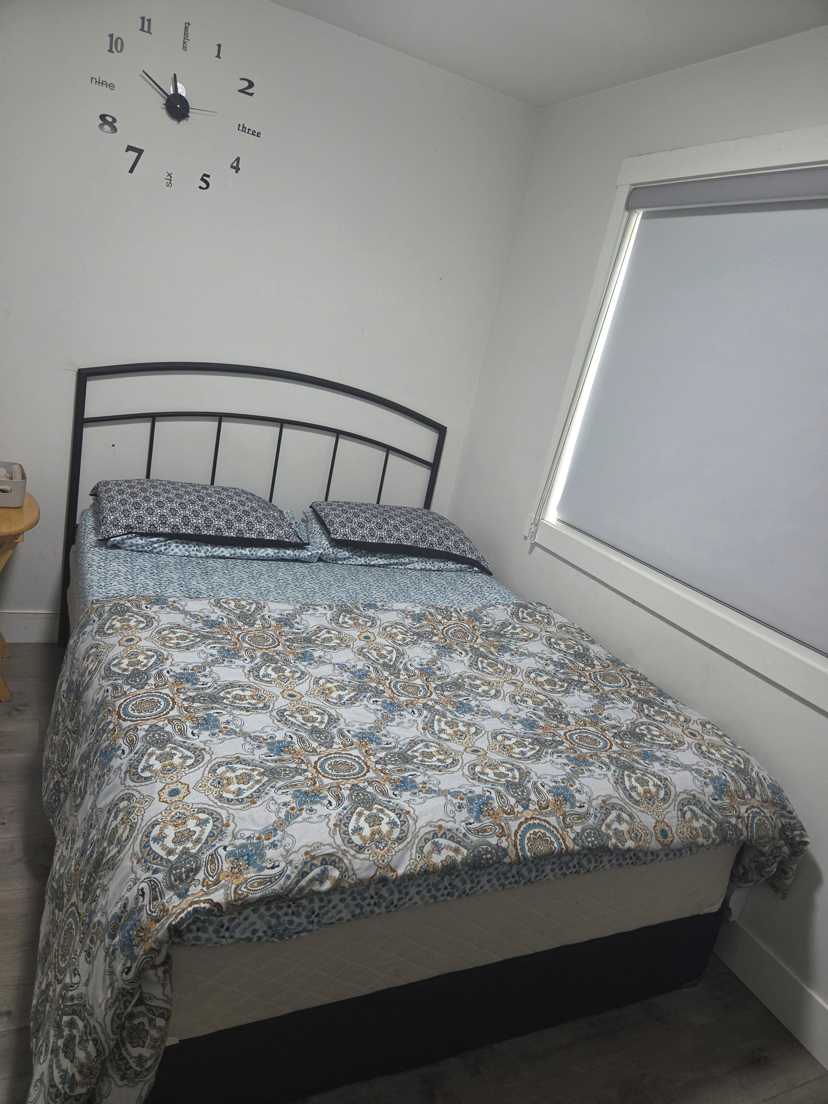 A bedroom with a bed, a wall clock, and a window.