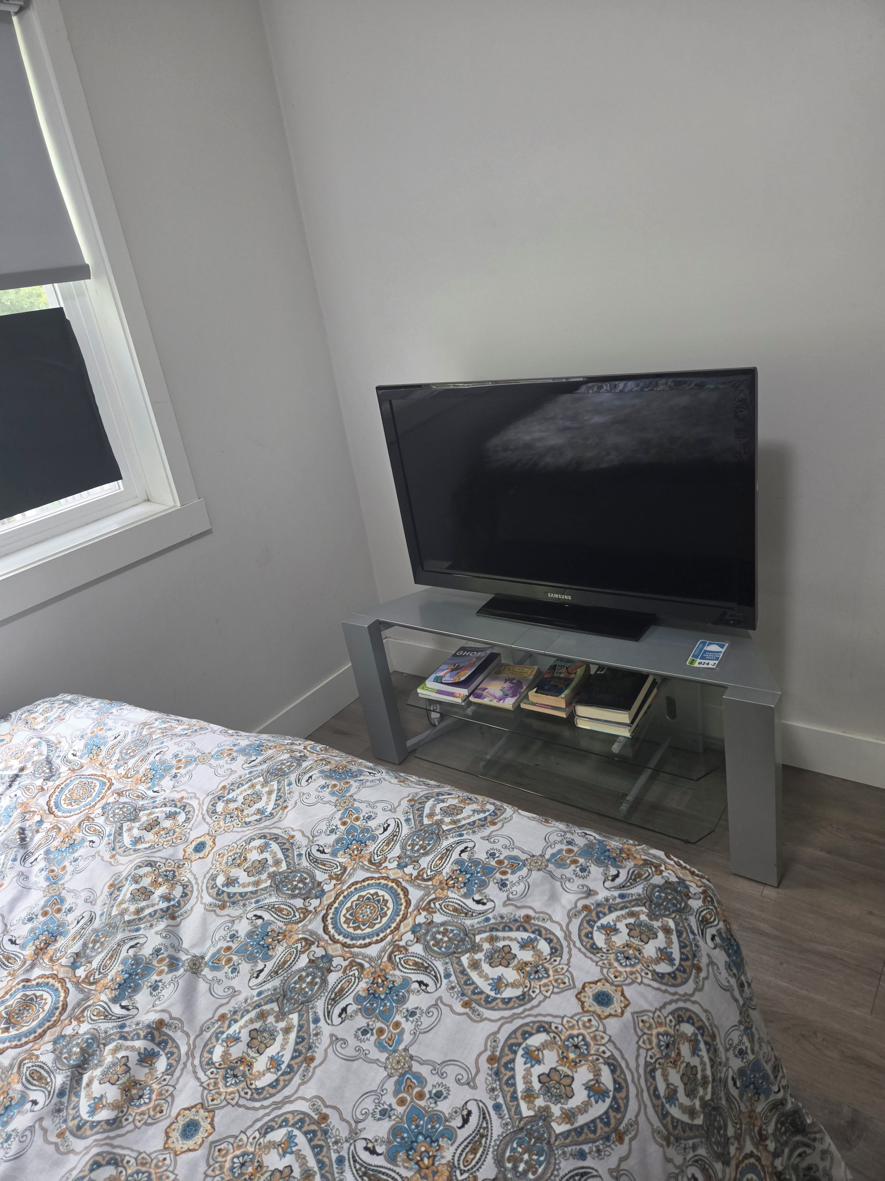A bedroom with a bed, a television on a stand, and a window with a curtain.
