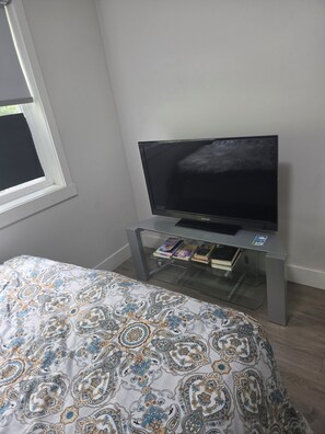 A bedroom with a bed, a television on a stand, and a window with a curtain.