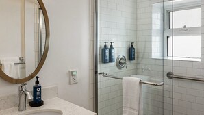 Ein Badezimmer mit einem runden Spiegel, einem Waschbecken mit Marmorplatte, einer Duschkabine aus Glas und einem Fenster.