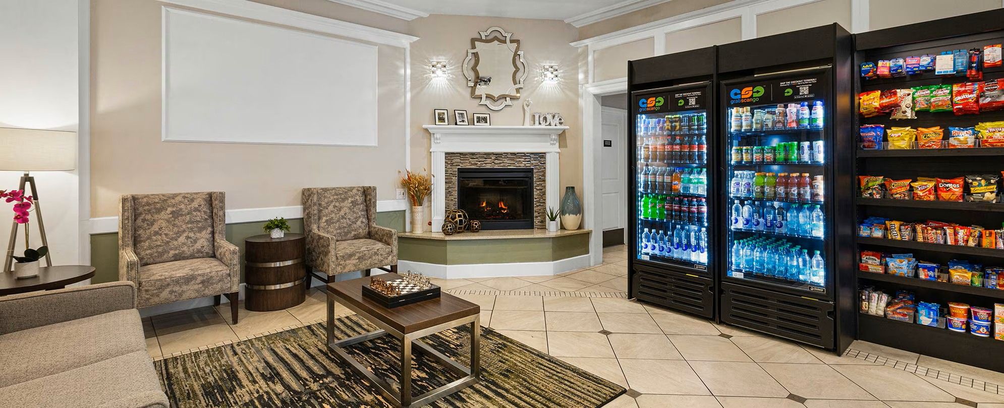 A hotel lobby with a fireplace, two armchairs, a coffee table, and a snack vending machine.