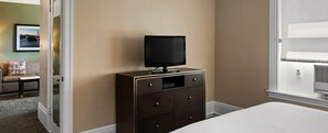 A hotel room with a bed, a dresser, a television on top, and a window with blinds.