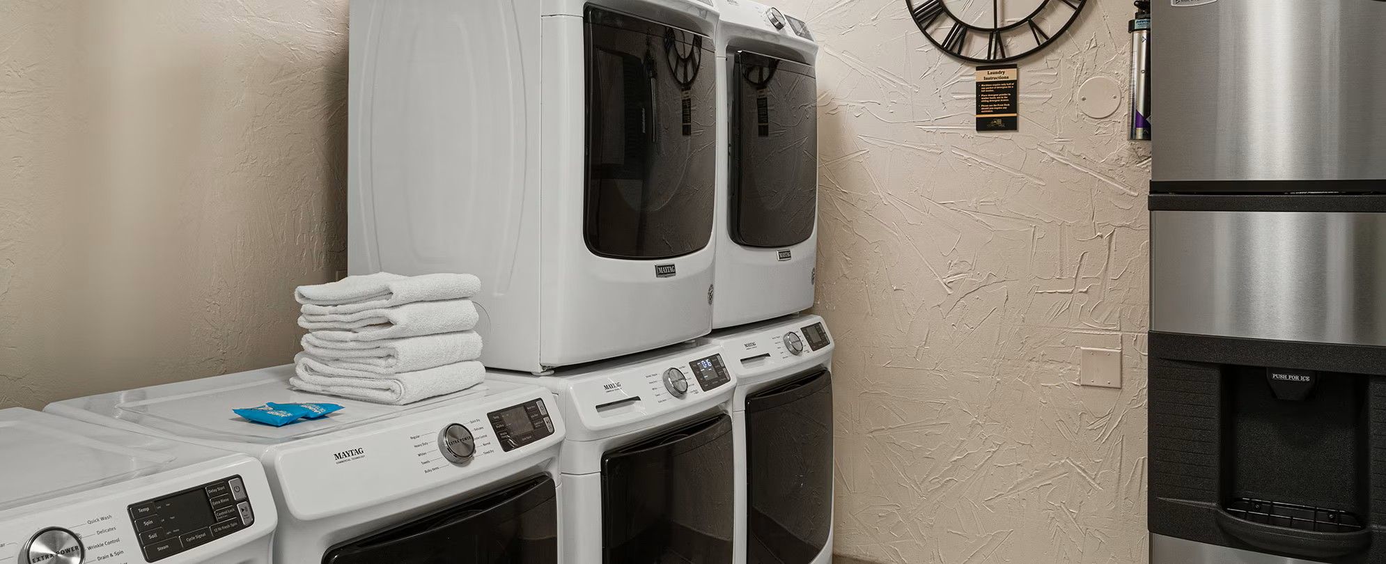 A laundry area with stacked towels, a Maytag dryer, and a stainless steel refrigerator.