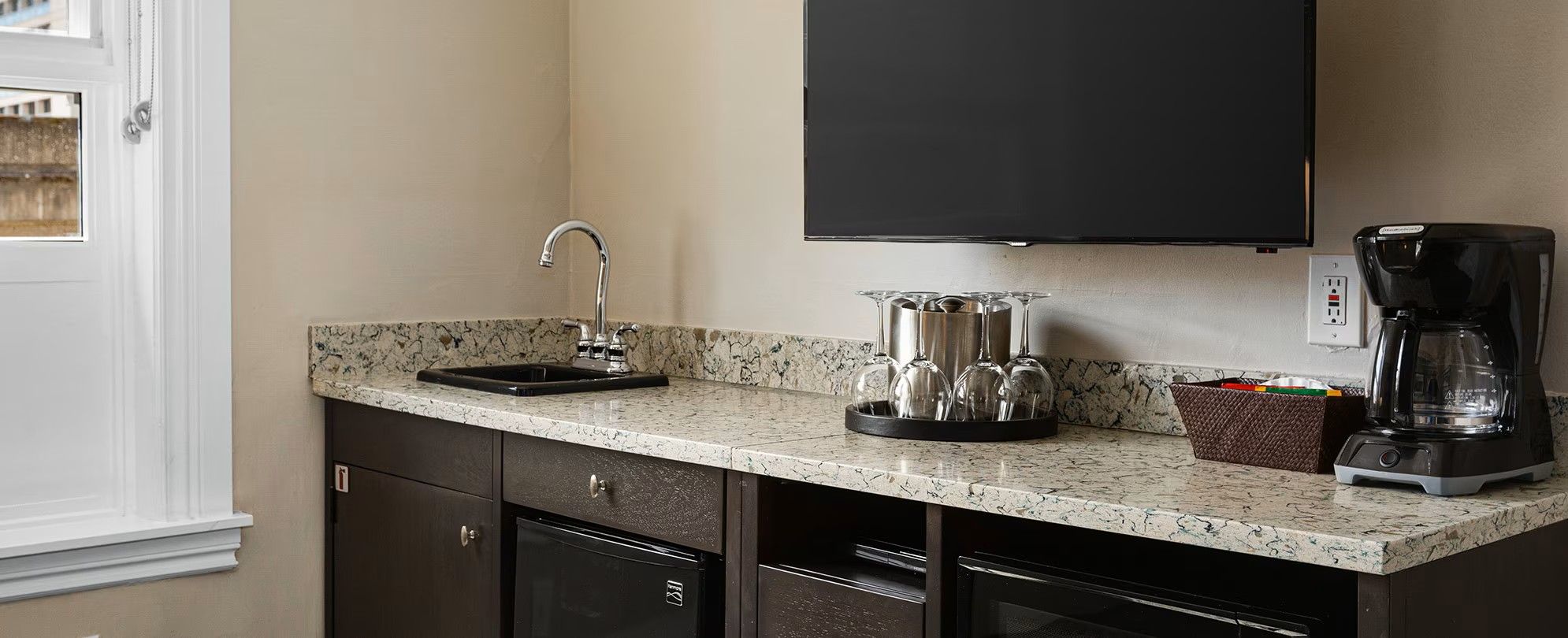 A kitchen with a granite countertop, a coffee maker, and a wine glass holder.
