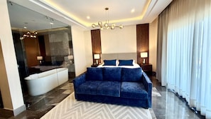 Ein modernes Hotelzimmer mit einem blauen Sofa, einer Duschkabine aus Glas und einem großen Fenster mit Vorhängen.