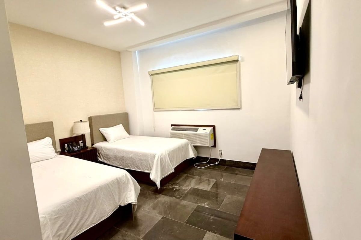 Ein Hotelzimmer mit zwei Betten, einem Schreibtisch, einem Telefon und einem an der Wand befestigten Fernseher.