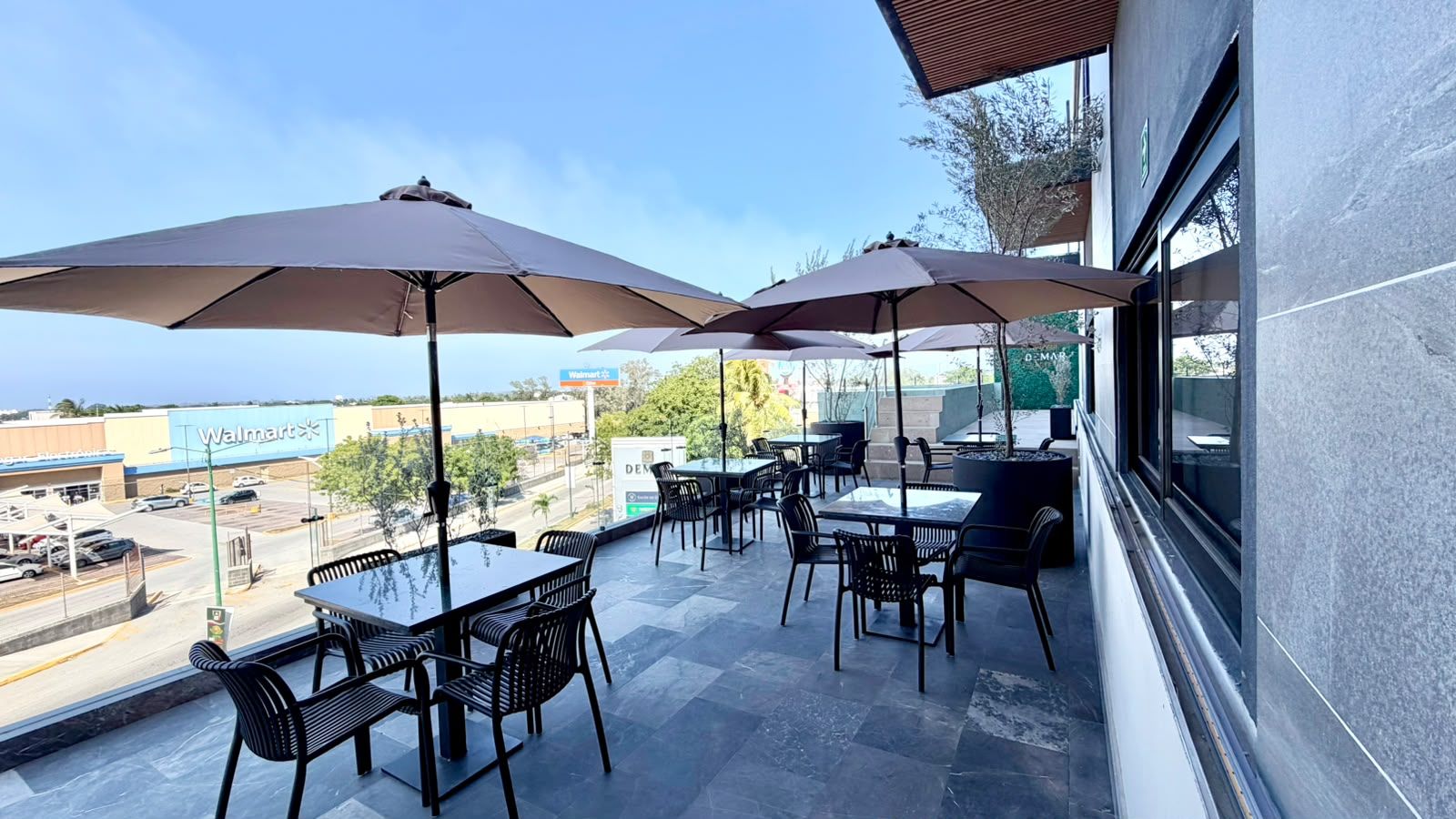 An outdoor patio with tables and chairs, umbrellas, and a view of a Walmart store.