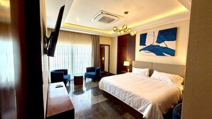 Una habitación de hotel con una cama, dos sillones, una mesita, un televisor y un cuadro en la pared.