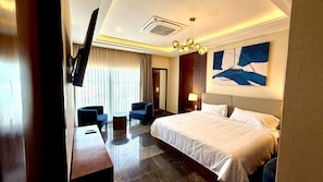 Ein Hotelzimmer mit einem Bett, zwei Sesseln, einem kleinen Tisch, einem Fernseher und einem Bild an der Wand.