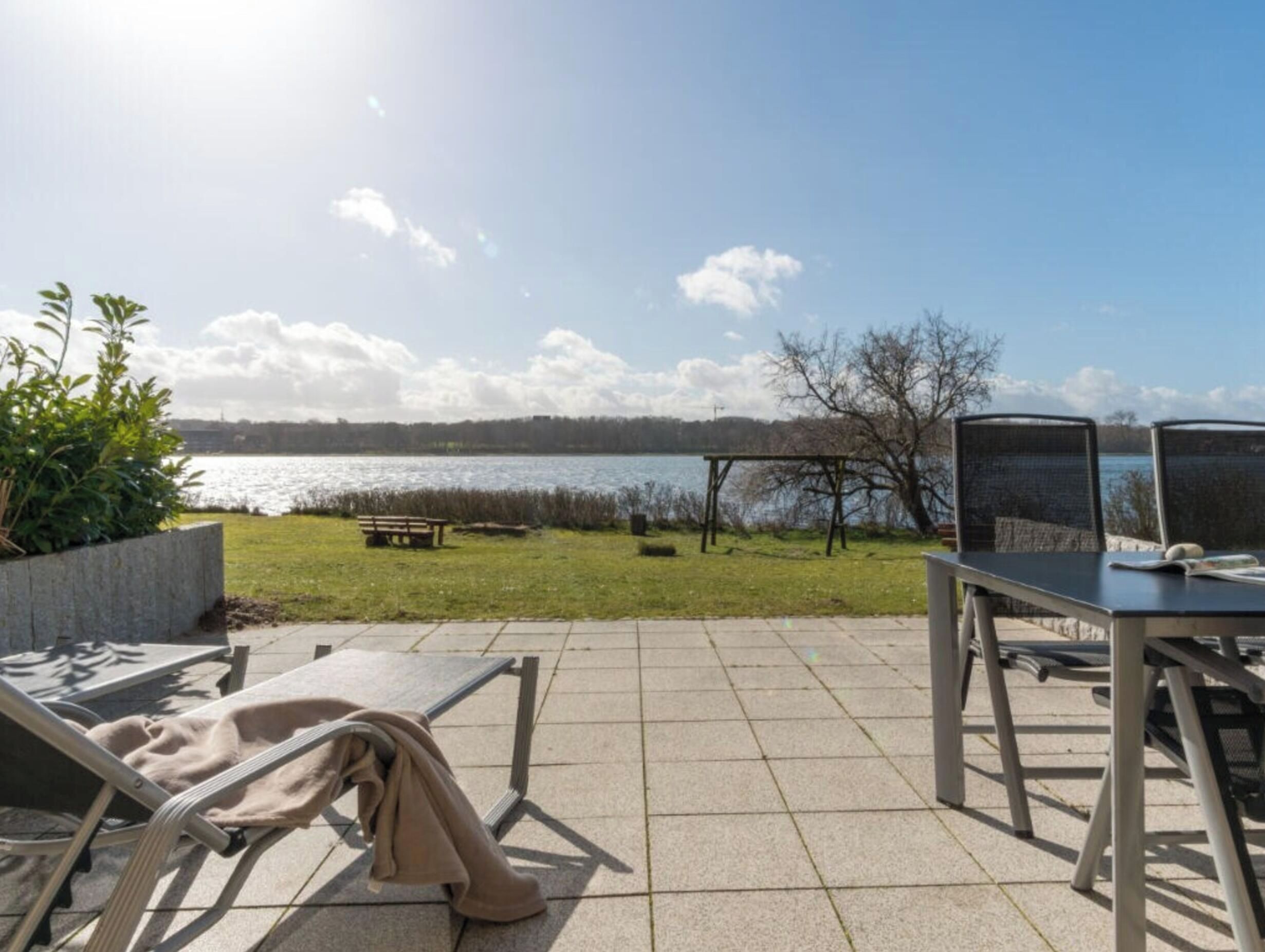 Un patio al aire libre con vista a un lago, una banca y una mesa con sillas.