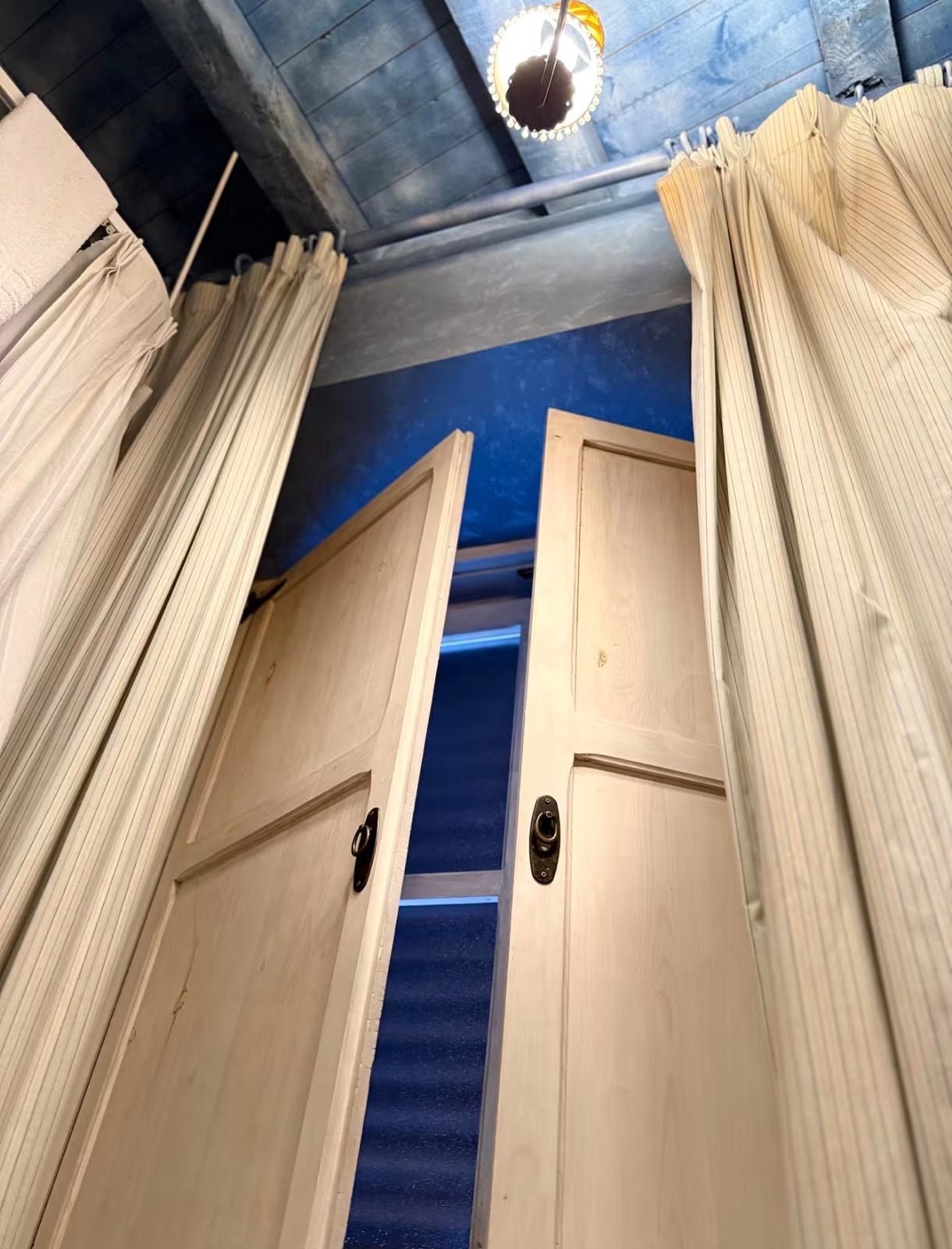 Una habitación con puerta de madera, alfombra azul y lámpara en el techo.