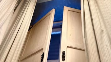 Una habitación con puerta de madera, alfombra azul y lámpara en el techo.