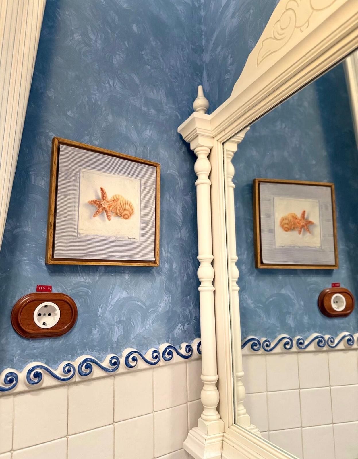 Een badkamer met blauwe wanden, witte tegels en afbeeldingen van zeesterren in lijsten.