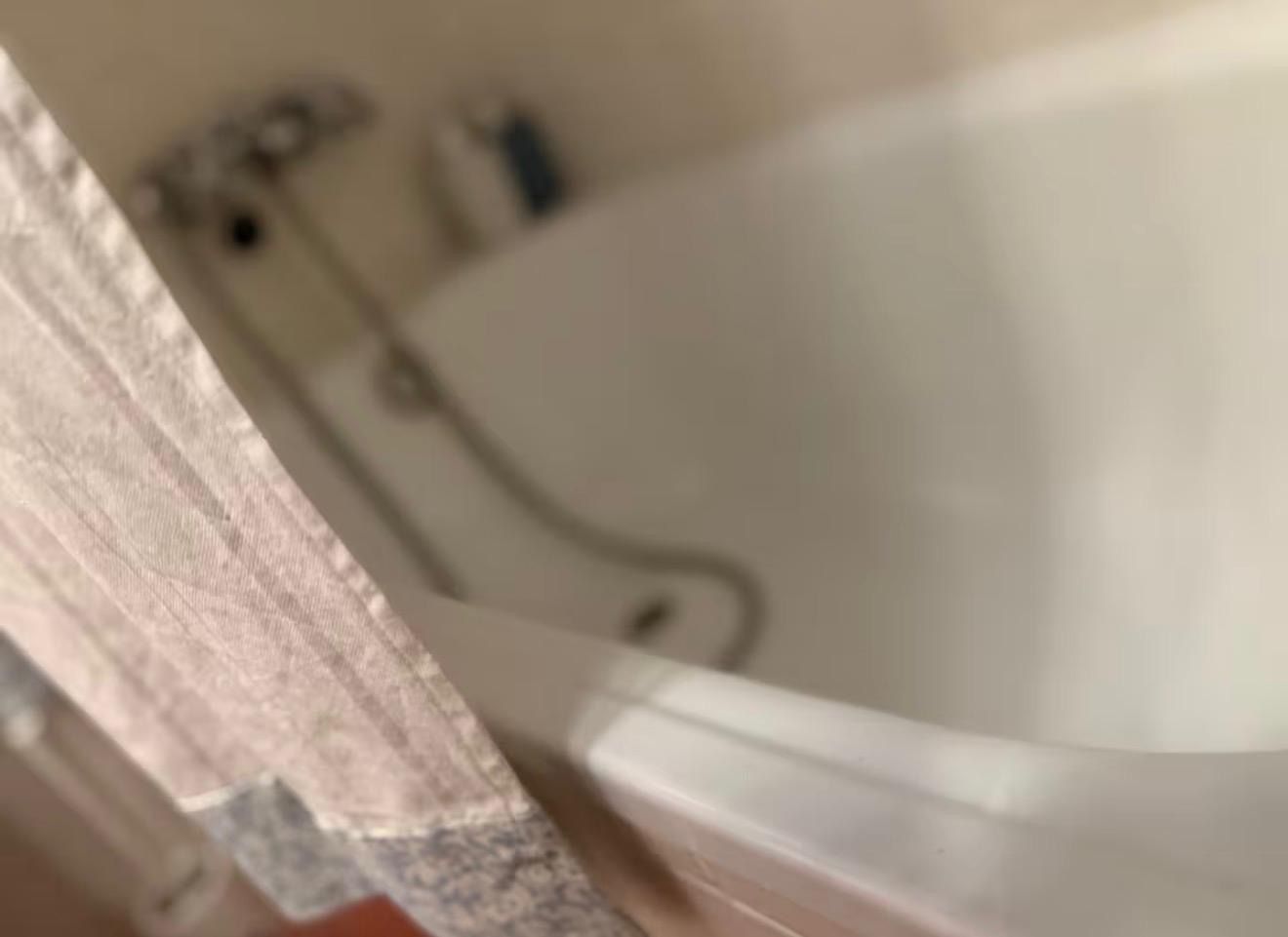 Una bañera con interior blanco, un cabezal de ducha y una cortina entreabierta.