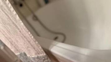 Una bañera con interior blanco, un cabezal de ducha y una cortina entreabierta.