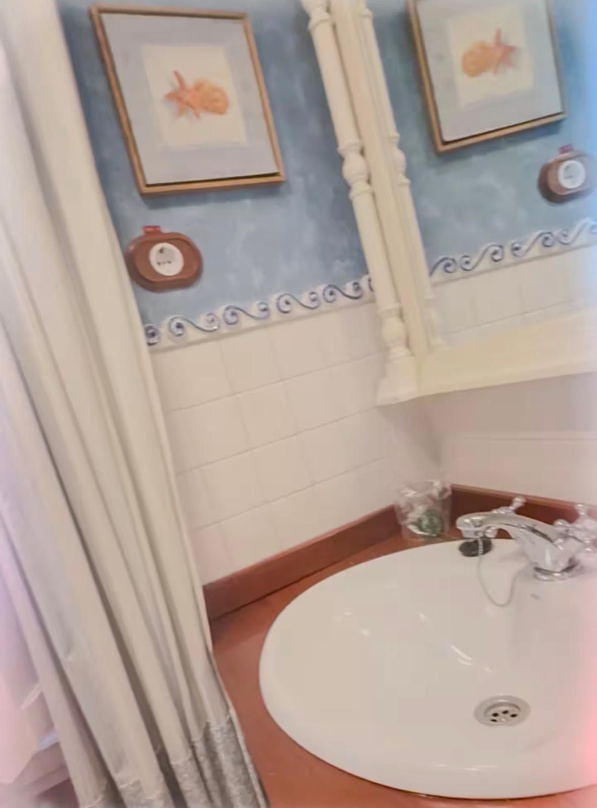 Et badeværelse med hvid vask, et spejl og billeder i rammer på væggen.