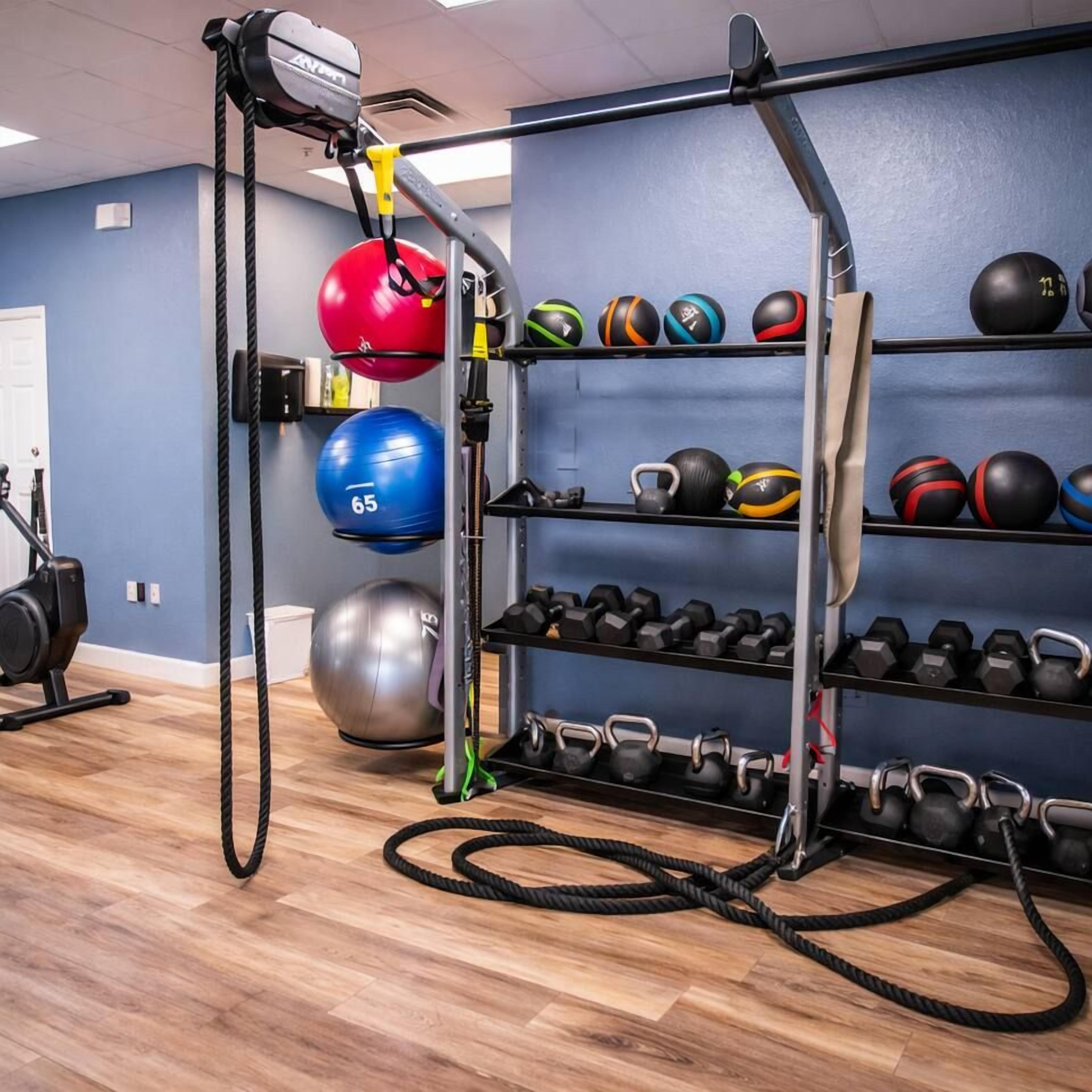 Un gimnasio con equipo de ejercicio, incluyendo una máquina de poleas, balones medicinales y mancuernas.