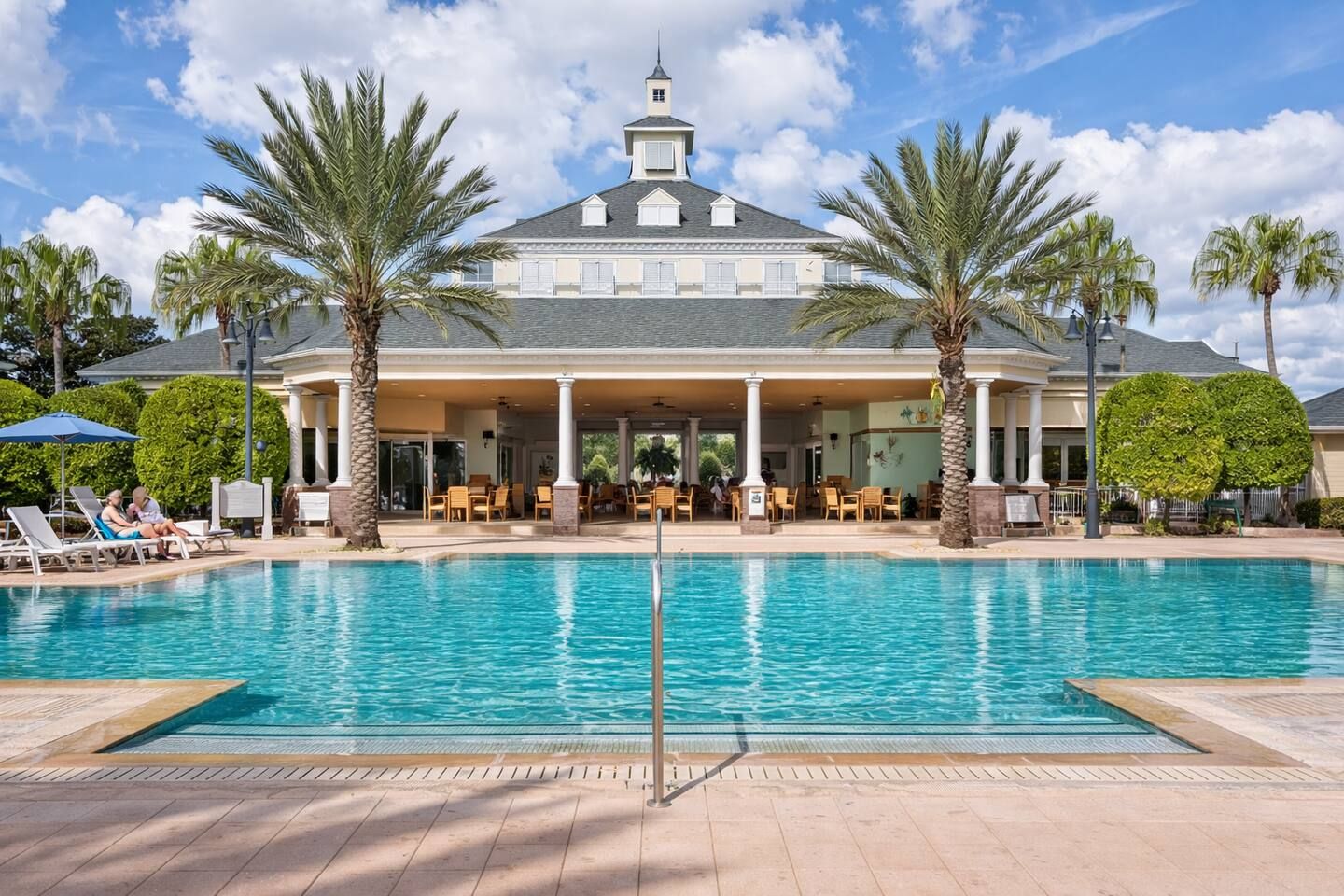 A hotel with a swimming pool, palm trees, and a covered outdoor seating area.