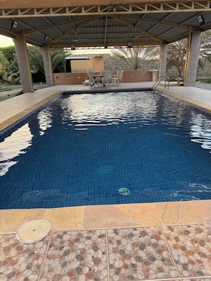 Piscina com deck revestido, área de estar coberta e parede de pedra ao fundo.
