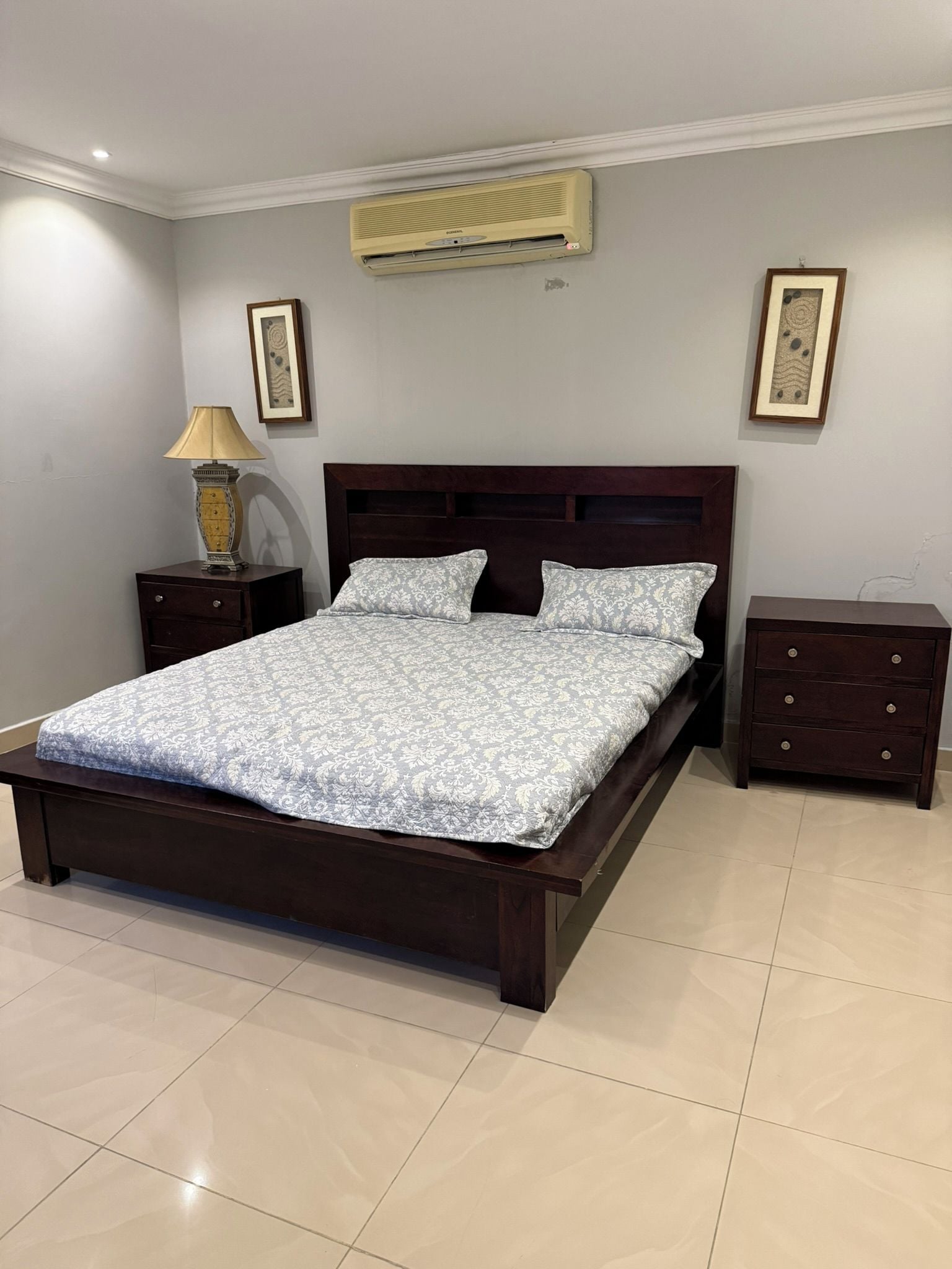 Een slaapkamer met een groot bed, een nachtkastje, een lamp en een dressoir.