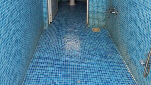 Un baño con paredes y suelo de azulejos azules, un inodoro, una ducha y una ventana con persianas.