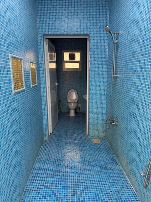 Casa de banho com azulejos azuis nas paredes e no chão, sanita, chuveiro e janela com persianas.