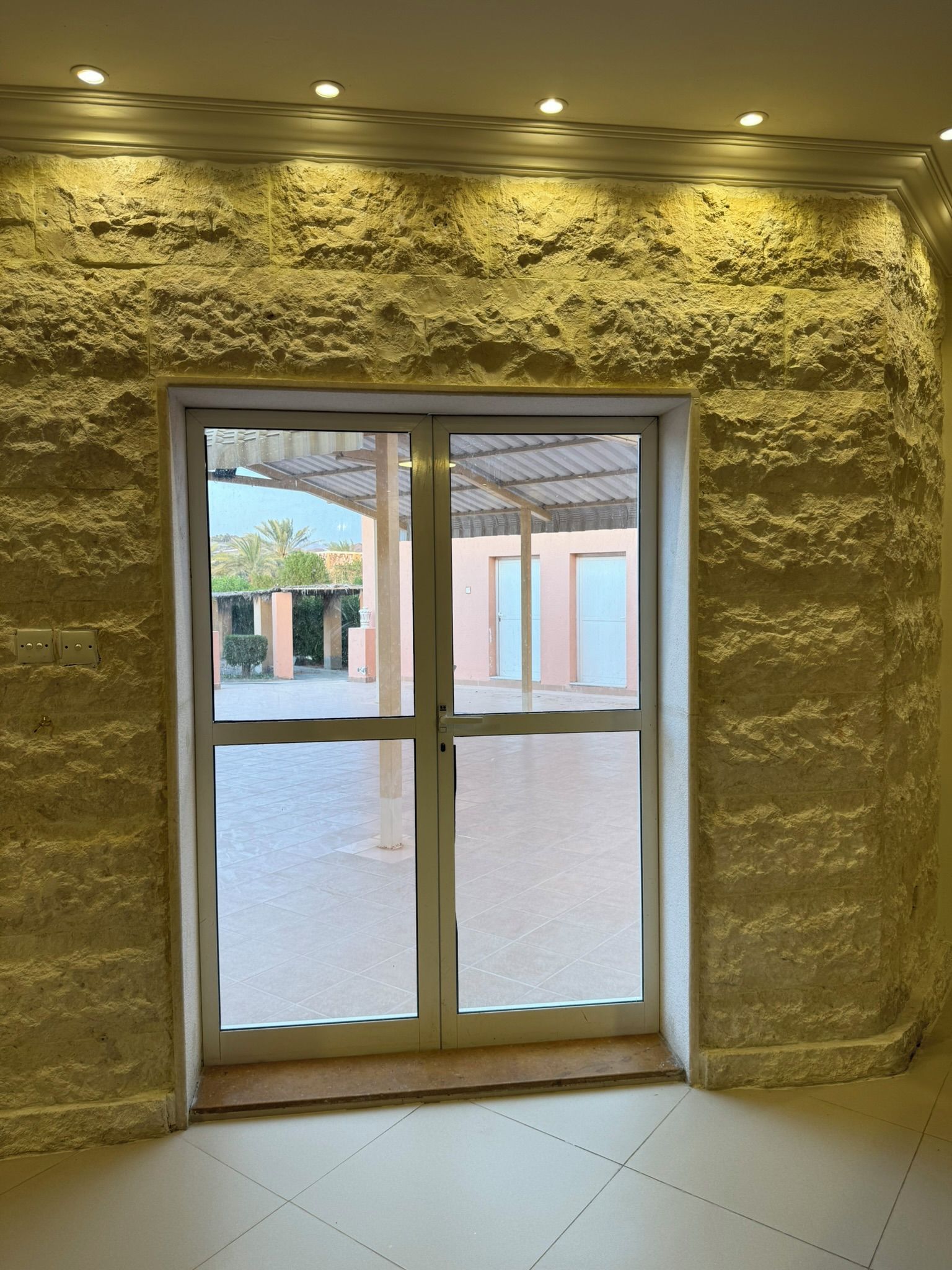 Una habitación con pared de piedra texturizada, un gran ventanal que da a un espacio exterior y suelo de baldosas.