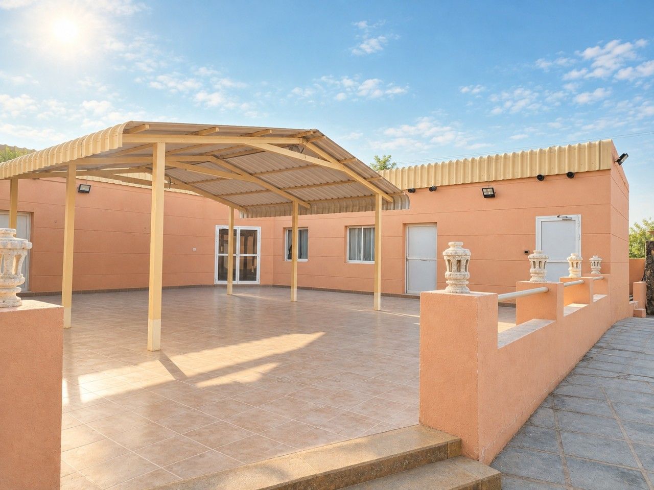 A covered outdoor area with a tiled floor, a wooden pergola, and a building with a flat roof.