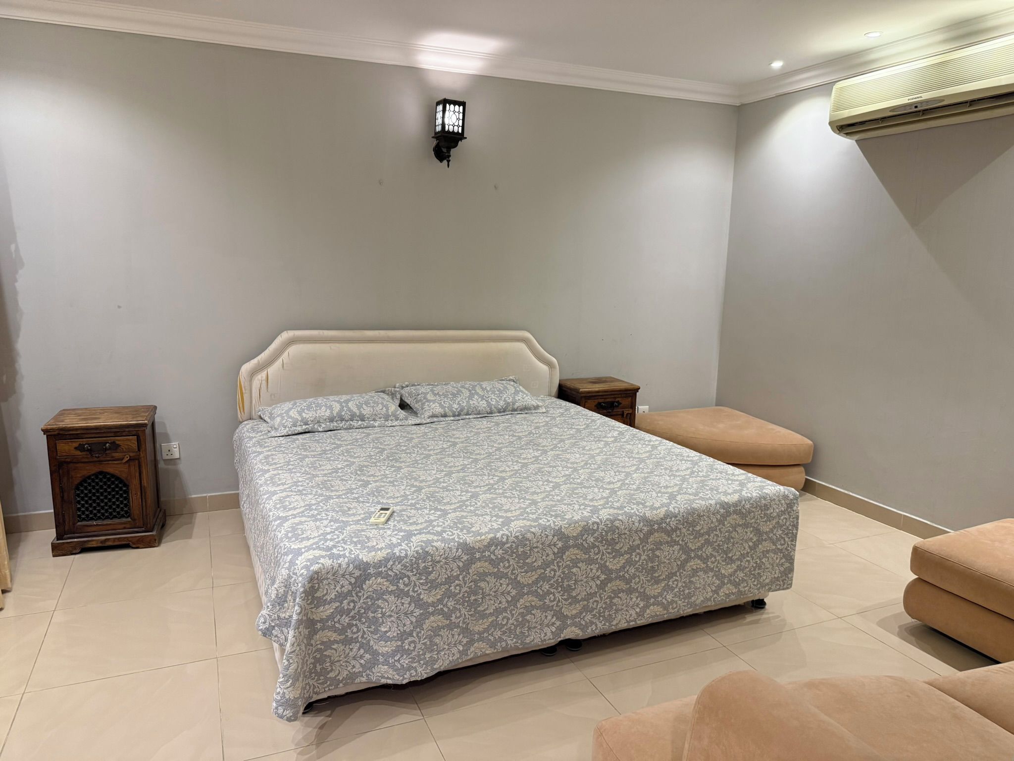 A bedroom with a bed, bedside tables, a nightstand, a bench, and a wall-mounted air conditioner.