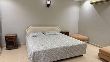 A bedroom with a bed, bedside tables, a nightstand, a bench, and a wall-mounted air conditioner.
