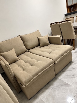 A beige sectional sofa with multiple cushions, a dining table with chairs, and a marble-tiled floor. - Cinema & Beach Experience • Exclusive Couple's Home (Rio das Ostras)
