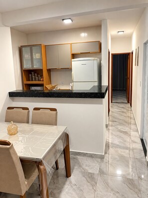 A modern kitchen with a refrigerator, cabinets, and a dining area with chairs and a table. - Cinema & Beach Experience • Exclusive Couple's Home (Rio das Ostras)