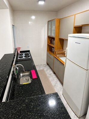 A compact kitchen with a gas stove, sink, and a white refrigerator. - Cinema & Beach Experience • Exclusive Couple's Home (Rio das Ostras)