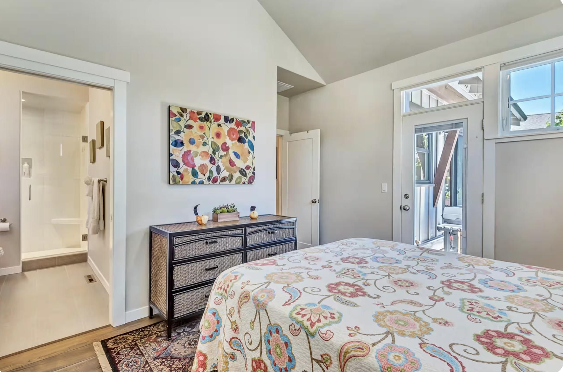 A bedroom with a bed, a dresser, a shower, and a door leading to a balcony.