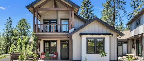 Une maison à deux étages avec un balcon, une véranda à l’avant avec des chaises et un petit garage attenant.
