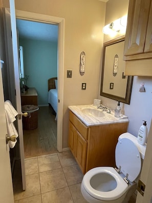 Un baño con inodoro blanco, lavamanos con encimera de mármol, armarios de madera y un espejo con marco decorativo.