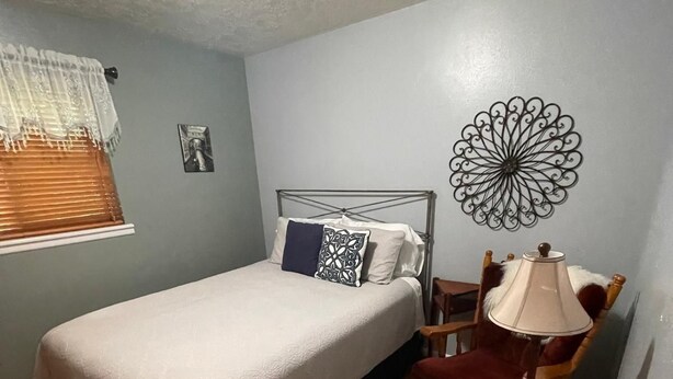 Een slaapkamer met een bed, een stoel, een lamp en een decoratief wandobject.