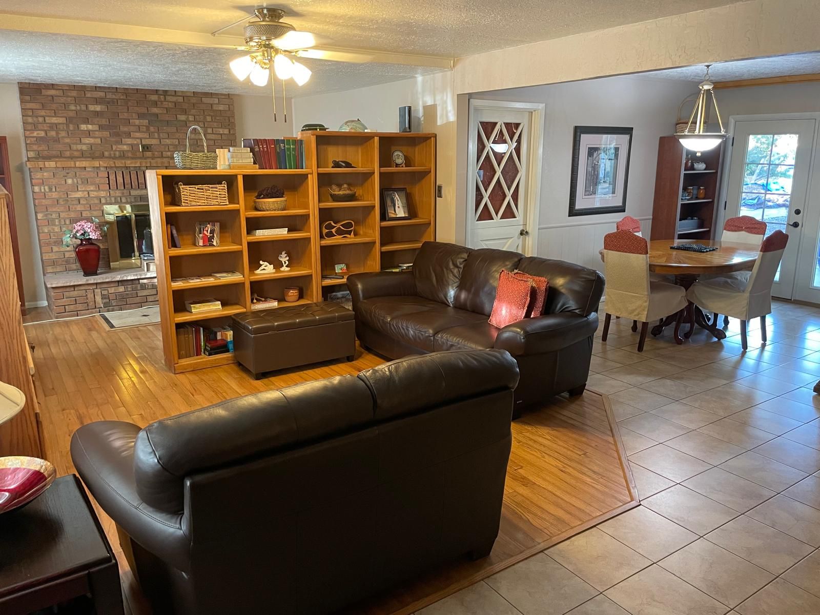 A living room with a leather sofa, a wooden bookshelf, and a dining area with a table and chairs.