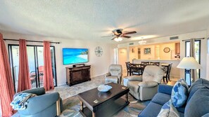 A living room with a television, seating, a ceiling fan, and a view through the glass door. - 2nd floor Serene Views updated Villa sleeps 8 (Panama City Beach)